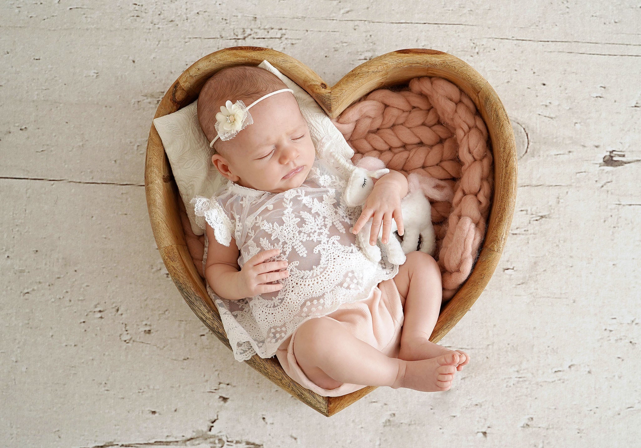 CUCOONU Baby in festlichem Outfit, liegend in einem Holzherz