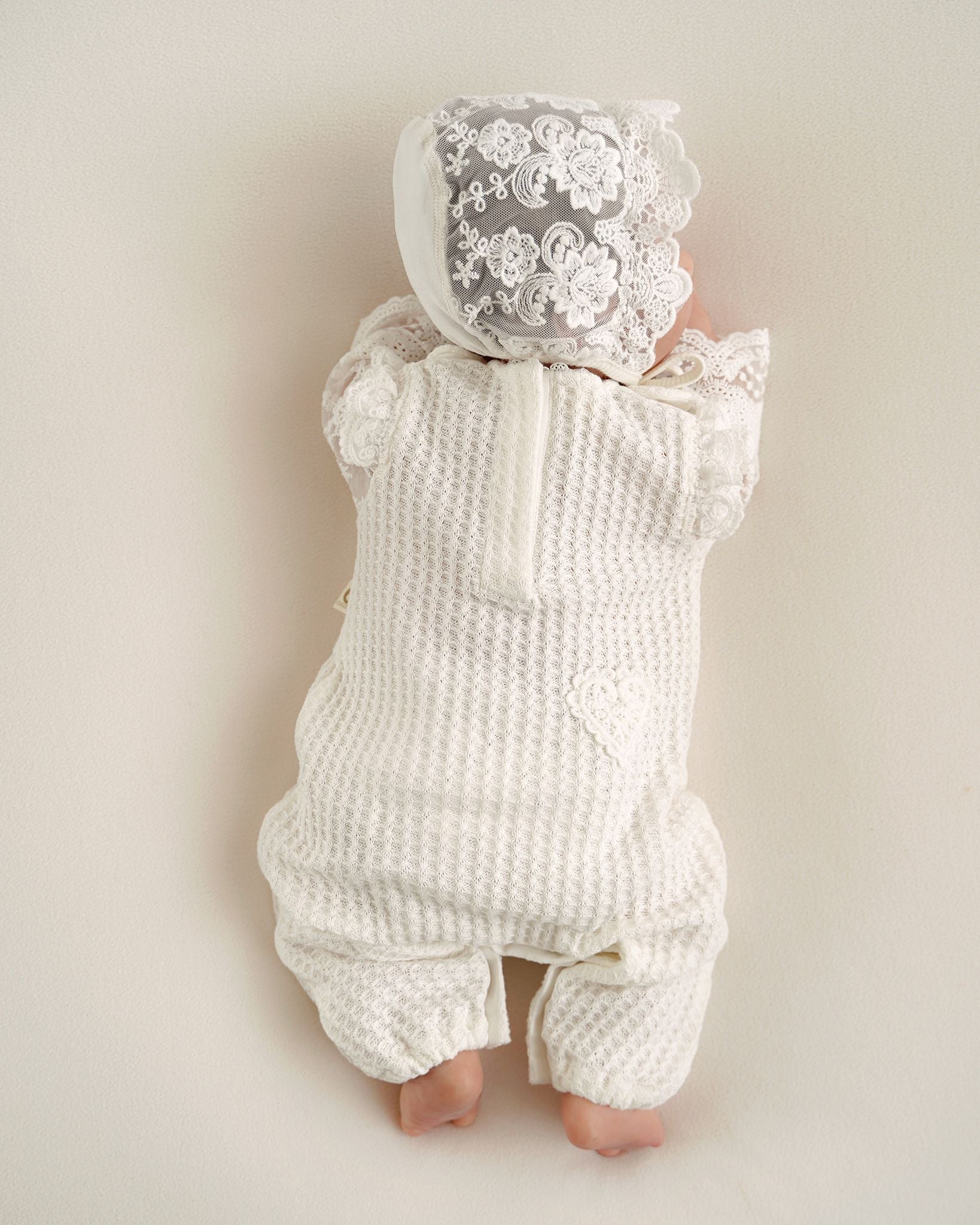 Baby trägt festlichen CUCOONU Strampler in Offwhite mit Herzdetail am Po, Rückenansicht