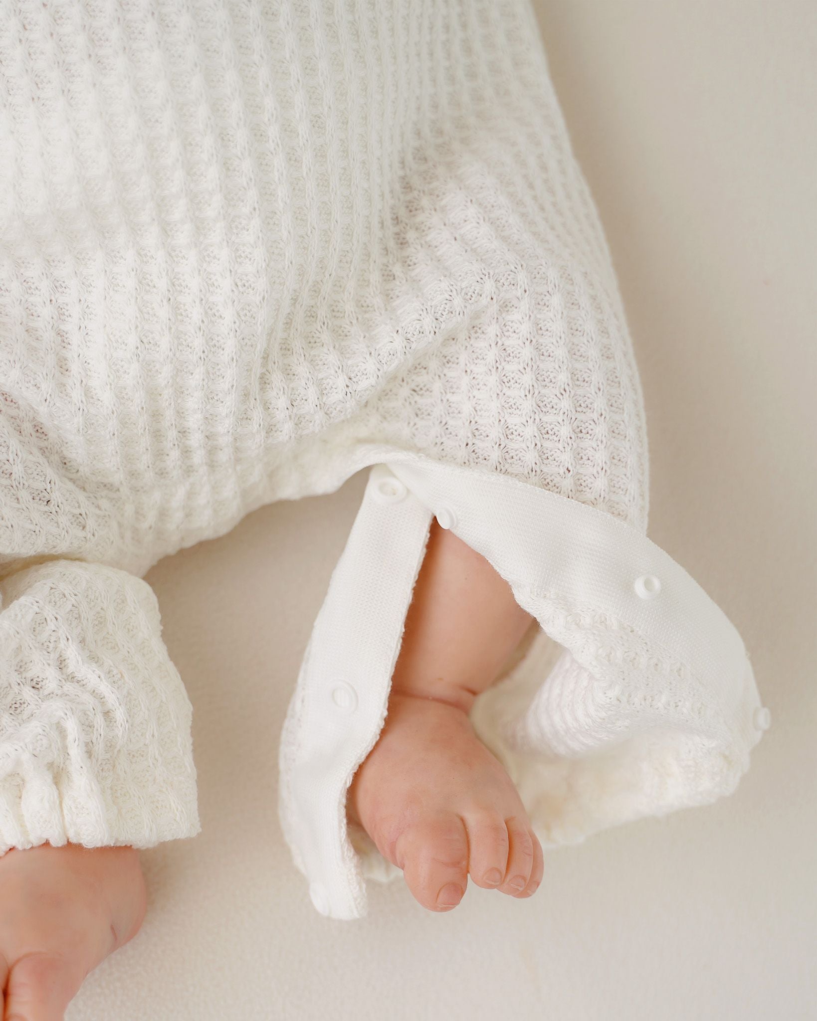 Festlicher CUCOONU Strampler in Offwhite, Detailaufnahme des Bodyverschlusses am Bein