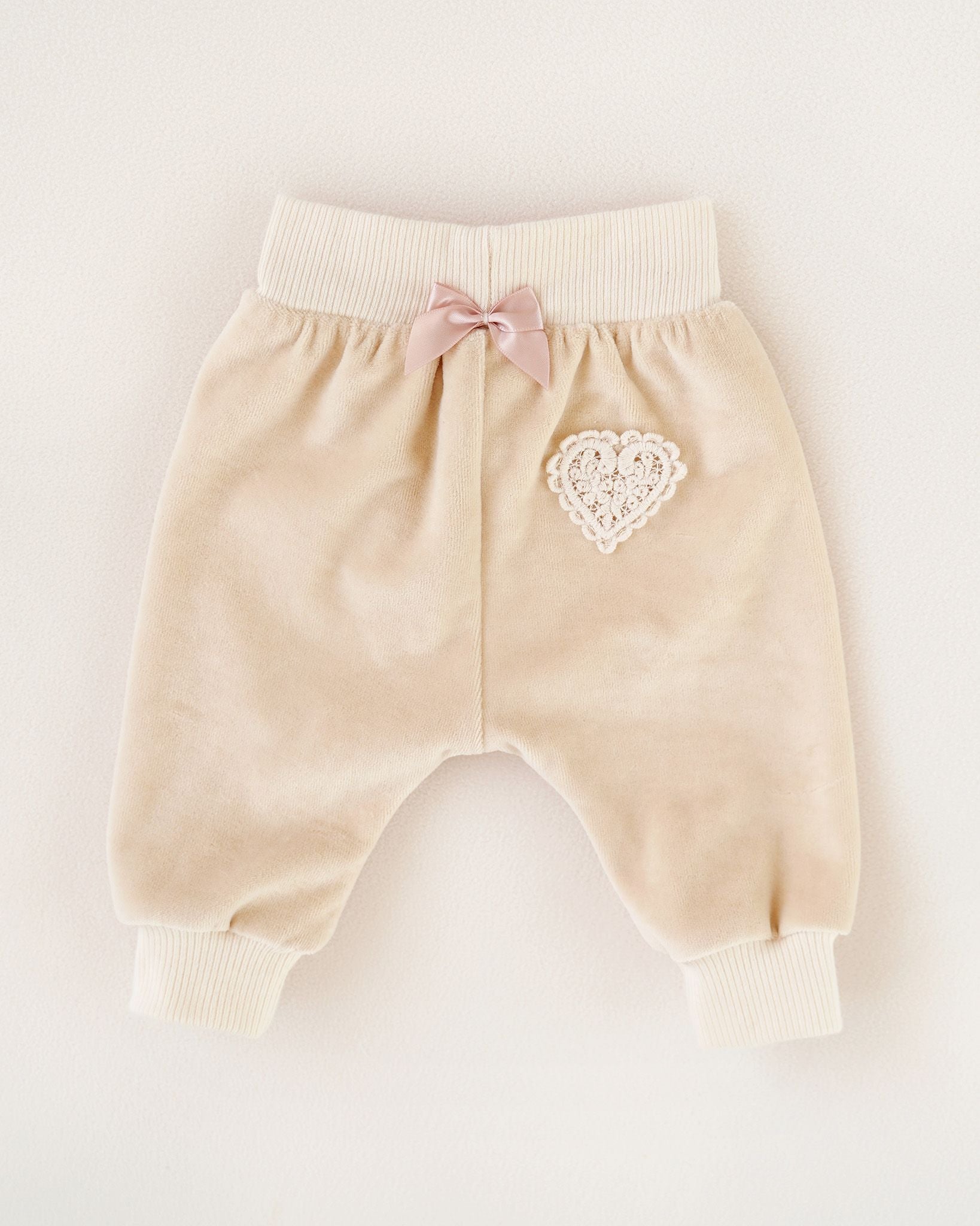 Rückenansicht einer CUCOONU Babyhose aus Samt in Beige mit Herzapplikation am Po und Schleife in Rosa