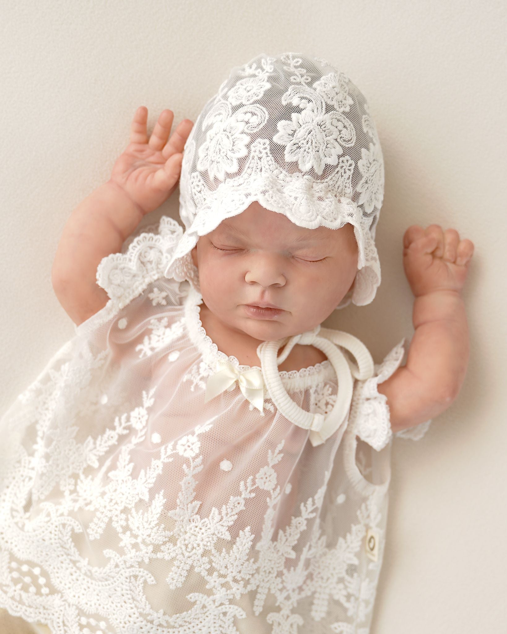 Neugeborenes Baby trägt ein festliches Cucoonu Spitzenkleid mit passender Taufmütze
