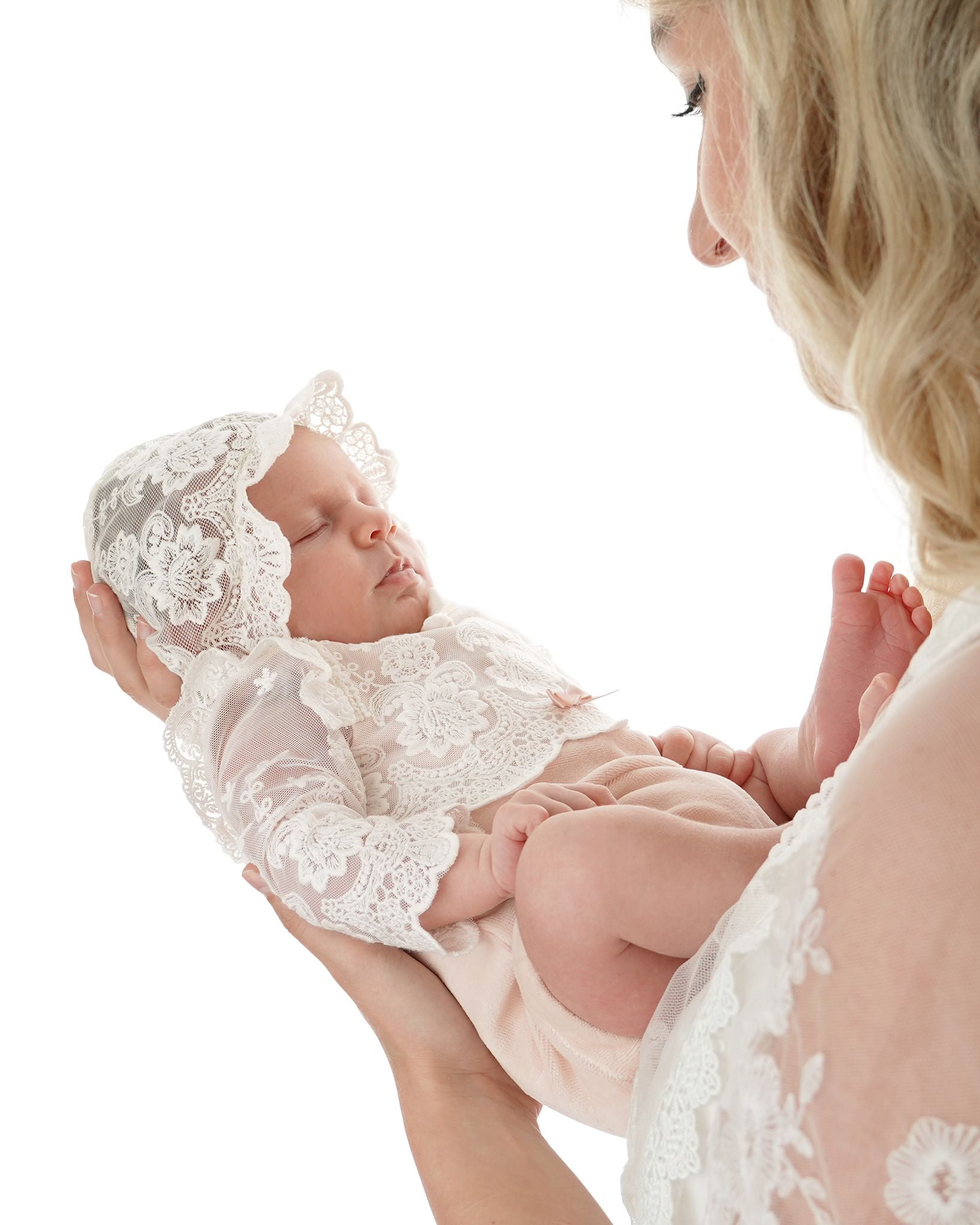 Neugeborenes Babymädchen trägt festlichen CUCOONU Body in Rosa mit Spitzenärmeln und Spitzenmütze, gehalten von Mama