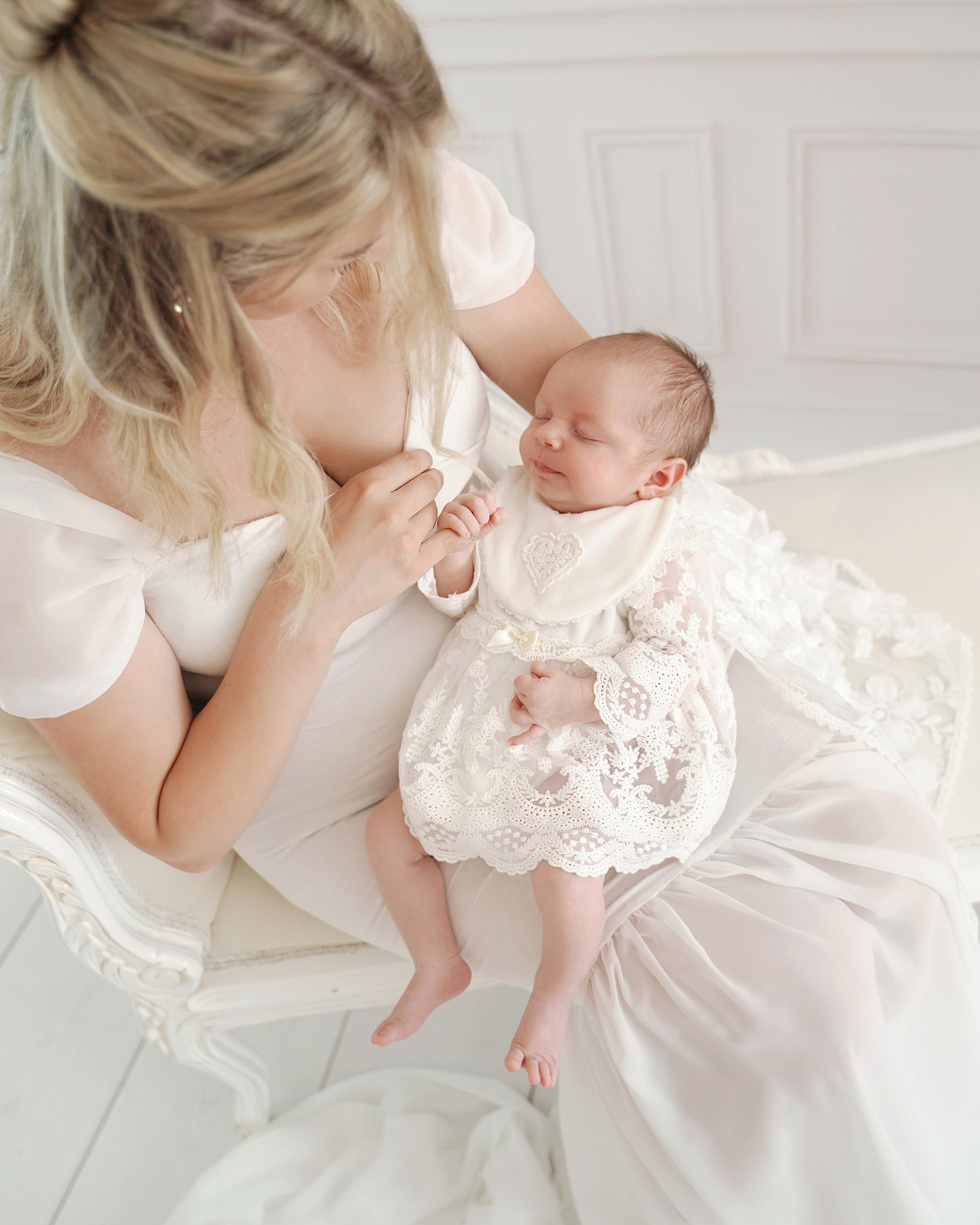Neugeborenes in CUCOONU Taufkleid hält Finger der Mutter, helle sanfte Farben