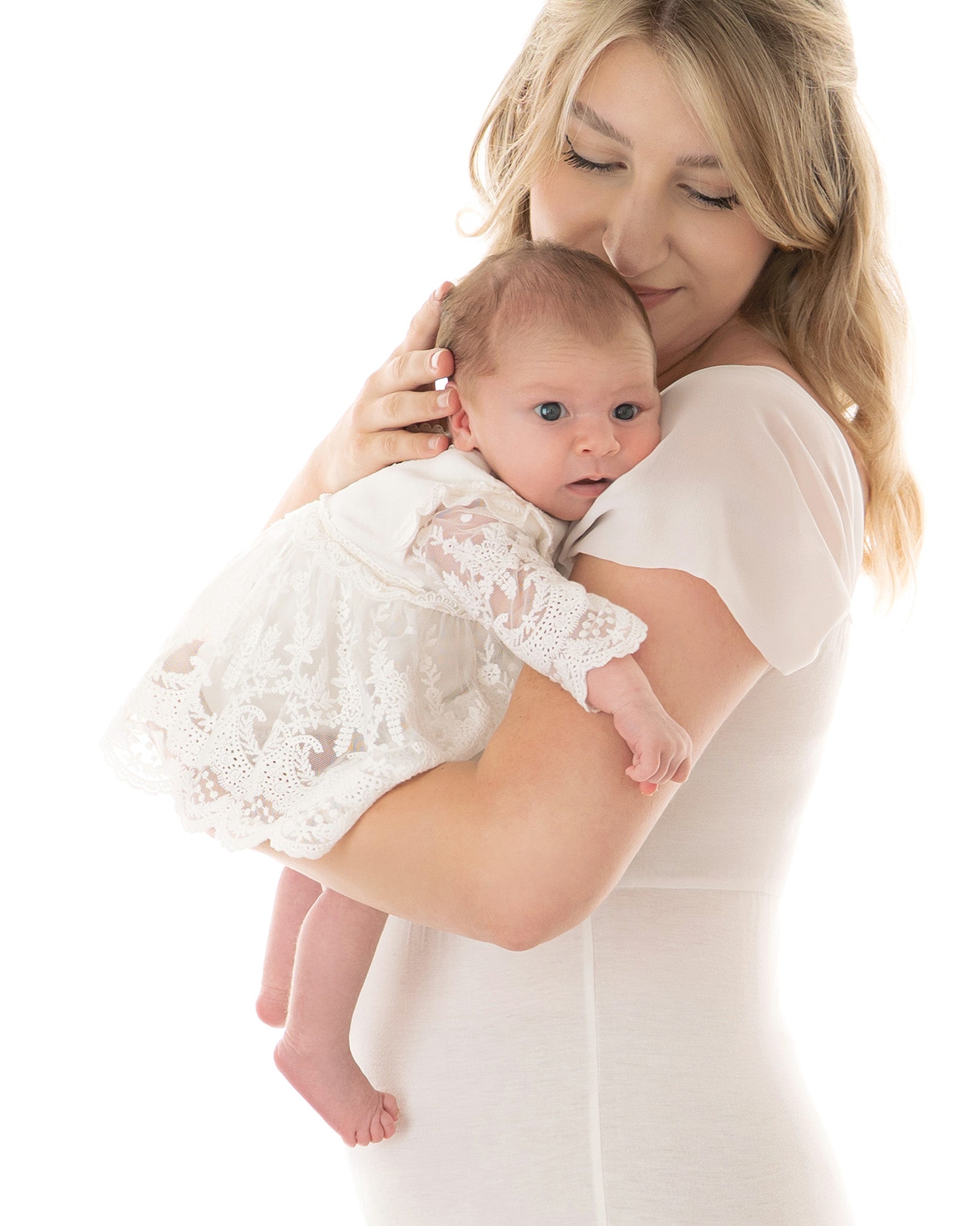 Neugeborenes Mädchen im zarten Spitzenkleid wird liebevoll von der Mutter auf dem Arm gehalten