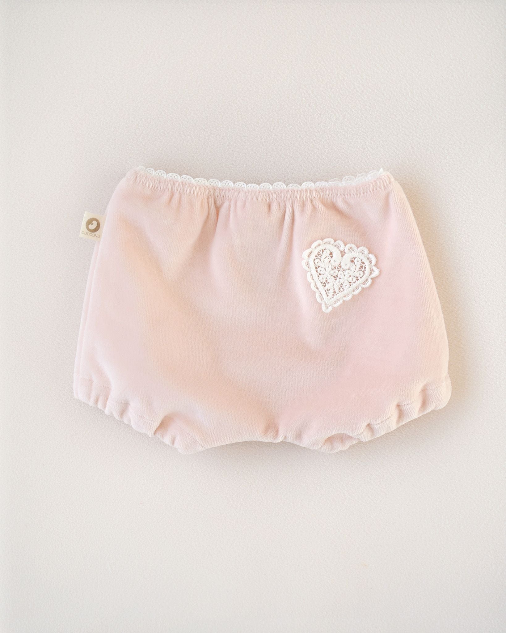 Rückenansicht eines CUCOONU Samthöschens für Baby in Rosa mit Herzapplikation am Po