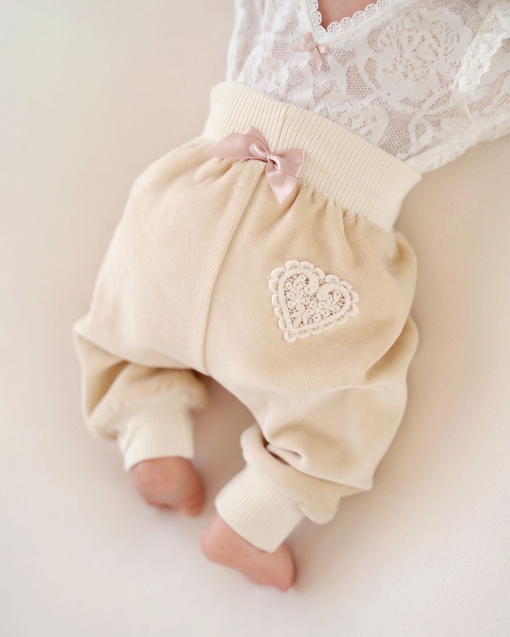 Baby trägt CUCOONU Babyhose aus Samt in Beige mit Herzapplikation am Po und rosafarbener Schleife, Rückenansicht