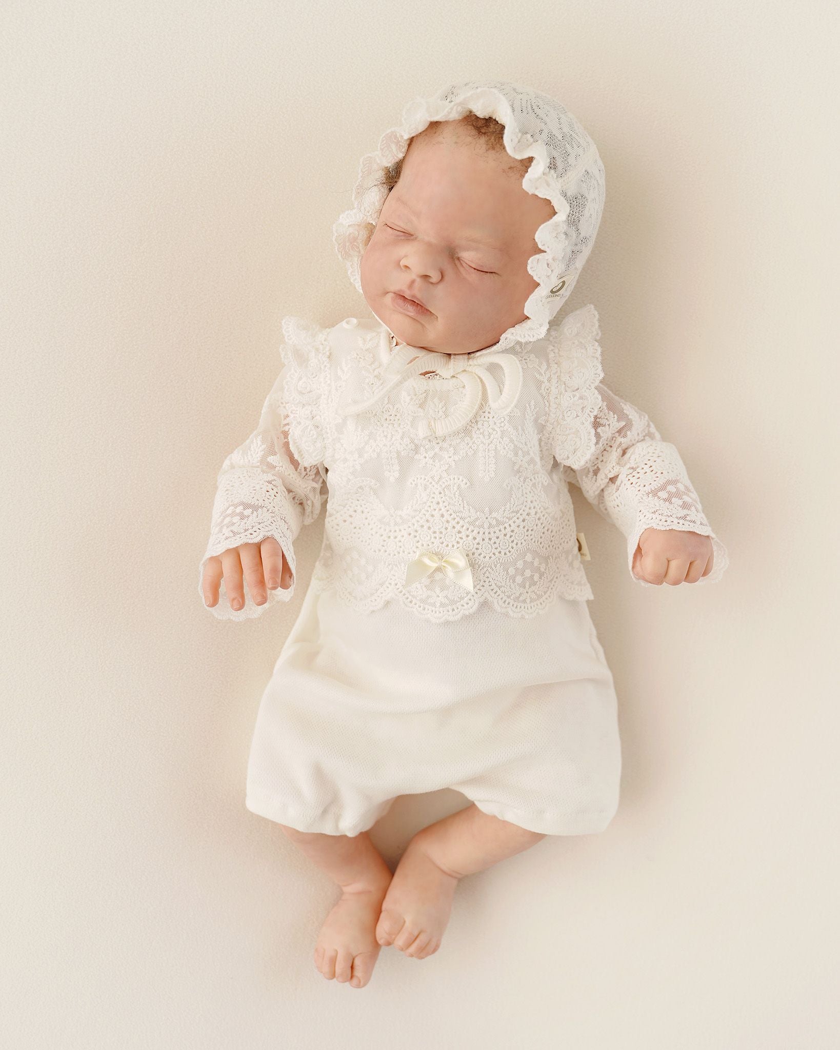 Neugeborenes Baby im festlichen CUCOONU Babybody mit Spitzenärmeln und passender Mütze aus Seiden-Jersey-Jacquard