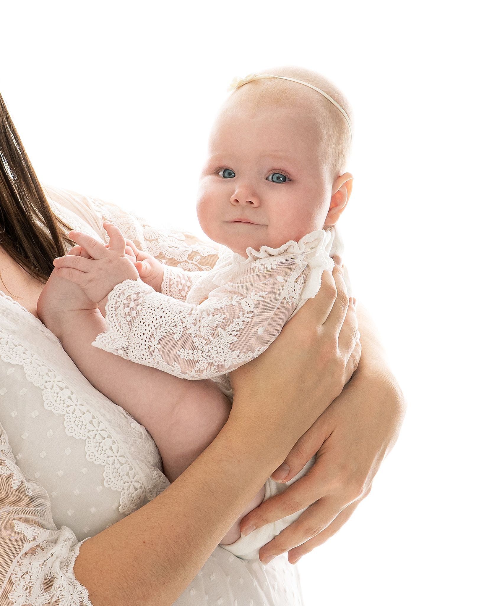Mamahände halten liebevoll ein Babymädchen in festlichem CUCOONU Body in Offwhite, Detailaufnahme