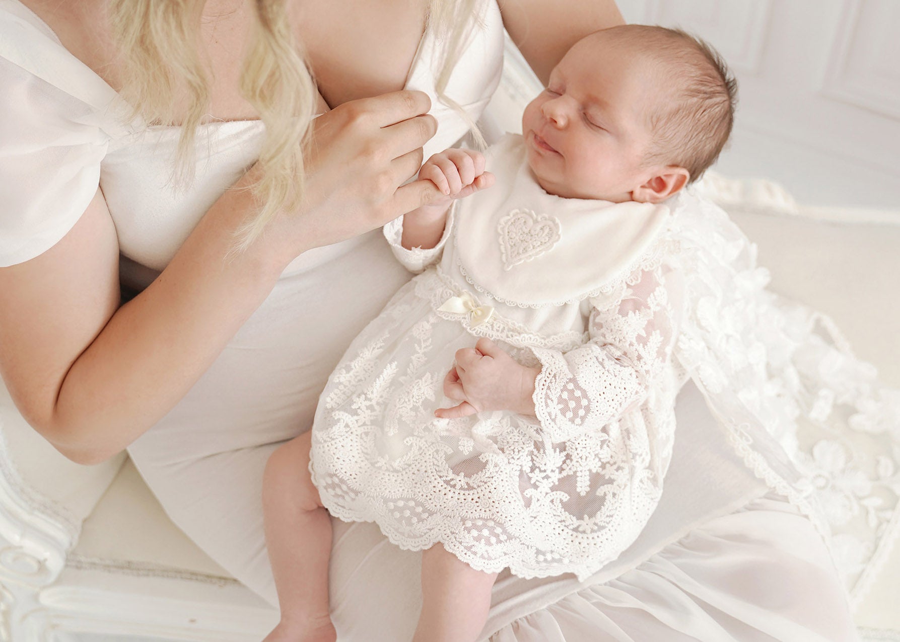 Baby schläft in einem Taufkleid und hält zart den Finger der Mutter